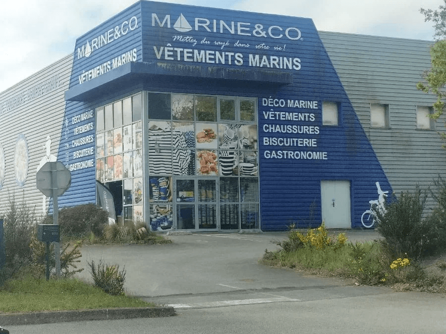 façade bleue d'un magasin Marine&Co avec vitrines et panneaux publicitaires pour vêtements marins et gastronomie